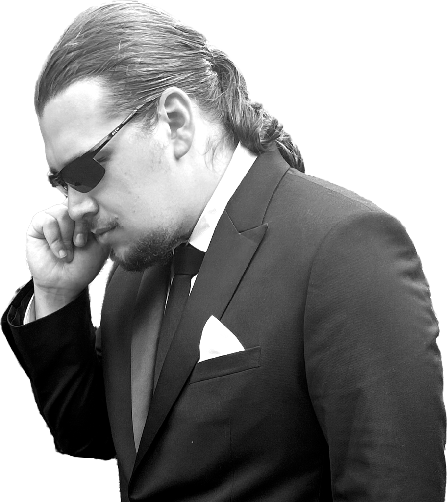 black and white photo of Emilio in a suit with sunglasses on holding his finger to his ear as if he's a secret service agent
